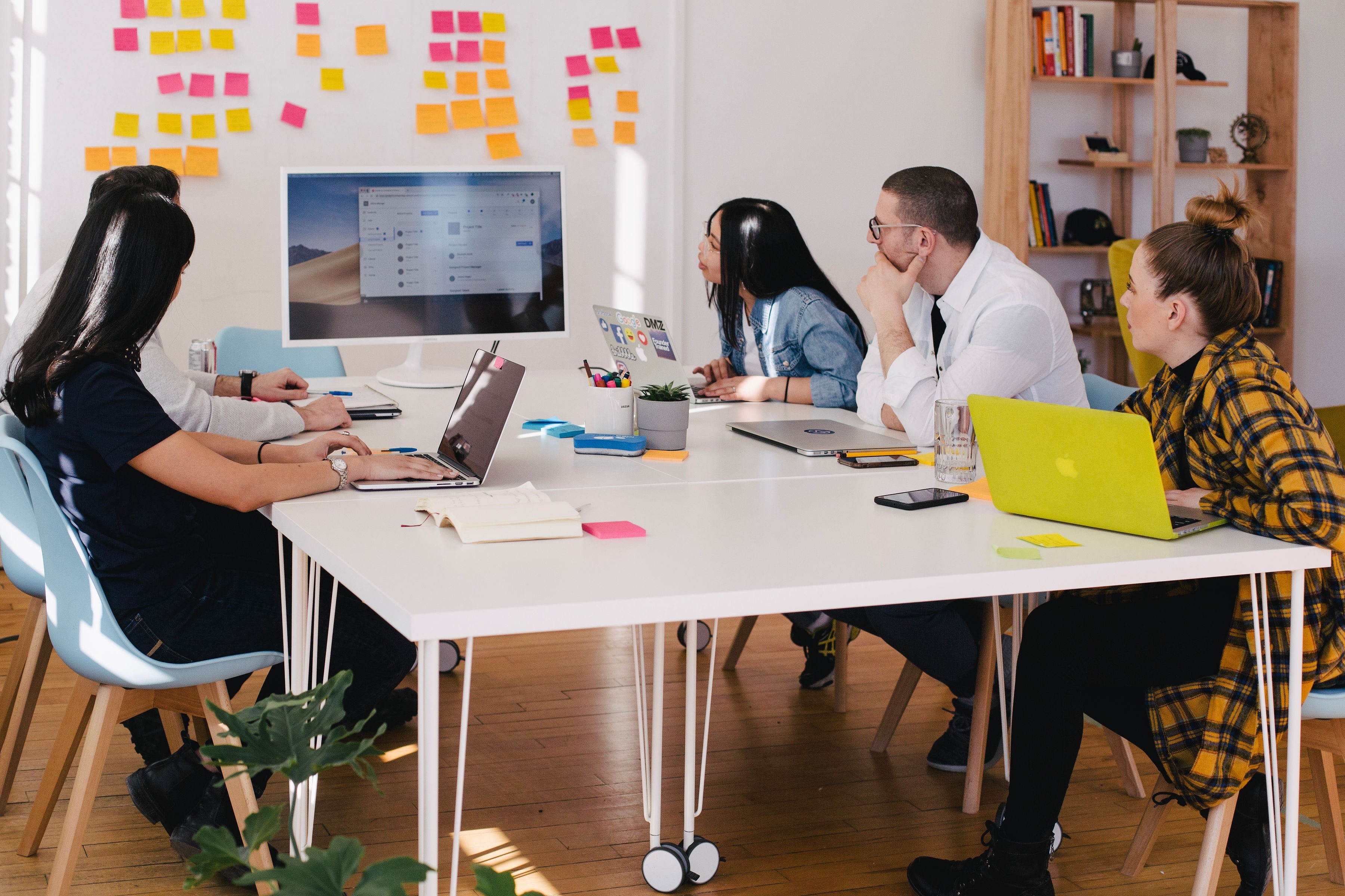 Equipe sentada em uma mesa branca olhando para um quadro com post-its coloridos criando um plano de redução de custos para a empresa.