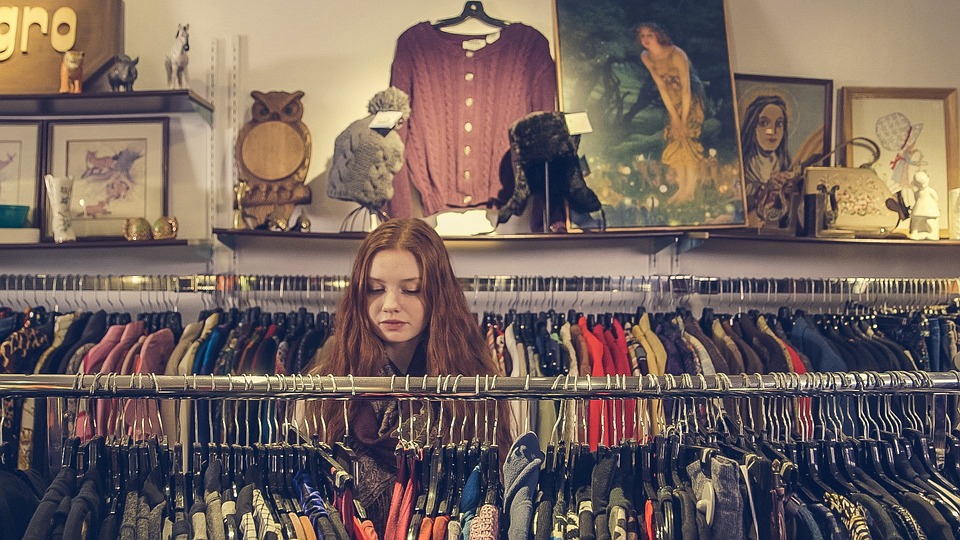Uma menina olhando peças de roupas em uma loja, representando o comportamento do consumidor.
