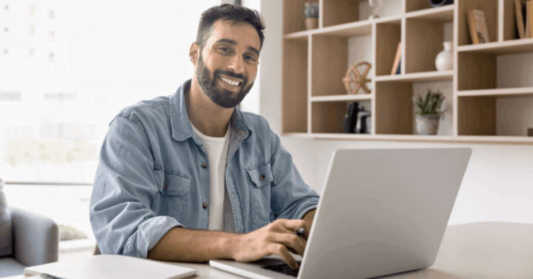 Profissional sorridente trabalhando em um notebook em ambiente de home office, representando o papel do PO (Product Owner) na gestão de produtos ágeis.