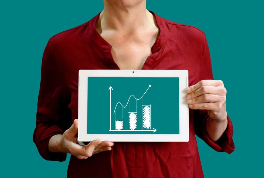 Na imagem, uma mulher segura um tablet com um gráfico de resultados positivos, representando bons resultados de uma boa gestão, proporcionados pelo conhecimento em ERP.
