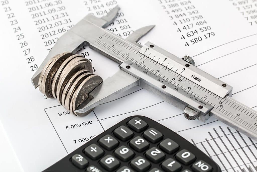 A precisão do acompanhamento das finanças da empresa está representada na imagem na figura de um paquímetro medindo um conjunto de moedas, sobre uma planilha contábil.