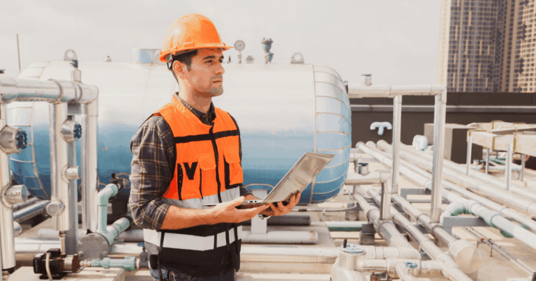 Técnico industrial utilizando notebook em área de produção para monitoramento e manutenção preditiva de equipamentos e tubulações.