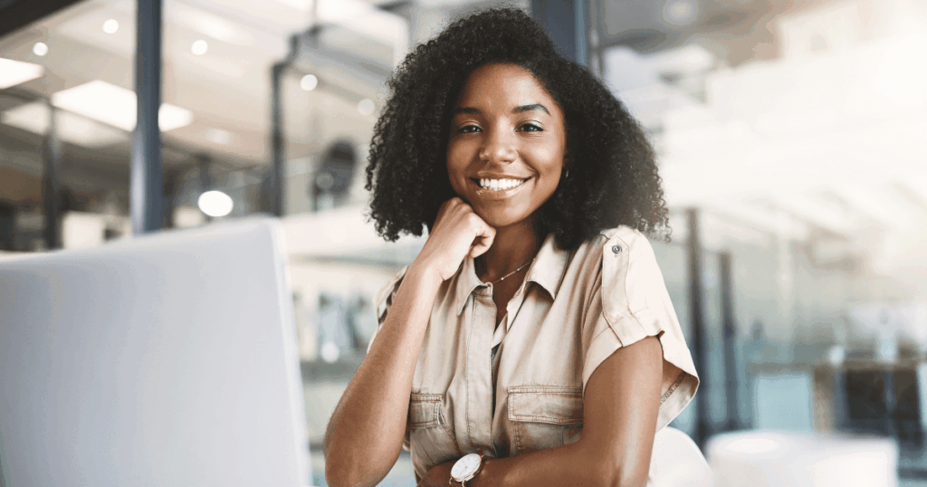 Mulher sorrindo em frente a um computador em um ambiente corporativo, representando a praticidade e eficiência do processo de admissão digital.
