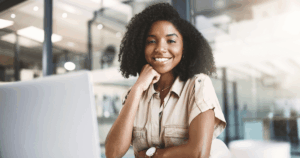 Mulher sorrindo em frente a um computador em um ambiente corporativo, representando a praticidade e eficiência do processo de admissão digital.