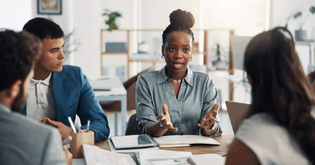 Equipe corporativa em reunião discutindo estratégias em ambiente de escritório moderno, com profissional apresentando ideias e colegas analisando informações, representando tomada de decisão em cenário complexo (mundo VUCA)