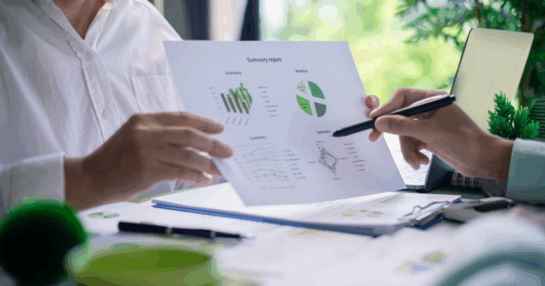 Duas pessoas analisando gráficos e relatórios impressos sobre desempenho e sustentabilidade em um ambiente de trabalho, representando o conceito de análise ambiental.