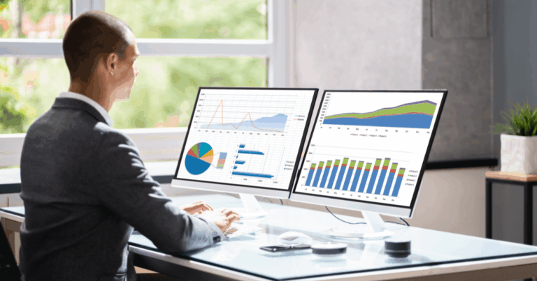 Profissional analisando gráficos e indicadores financeiros em dois monitores, representando o acompanhamento do ciclo operacional e do desempenho dos processos empresariais.