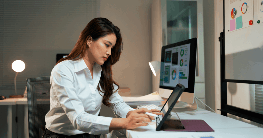 Mulher profissional sentada em um escritório moderno, analisando relatórios e gráficos financeiros em um tablet e monitor de computador, representando planejamento estratégico e benefícios EIP.