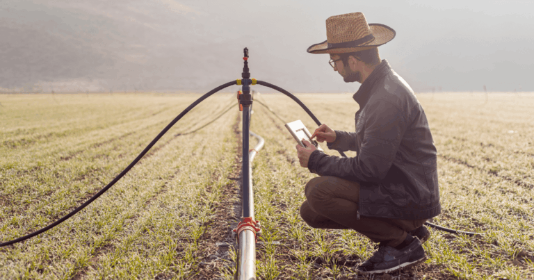 Agricultor utilizando tablet para monitorar sistema de irrigação em lavoura, representando práticas de agricultura moderna e uso de tecnologia no campo.