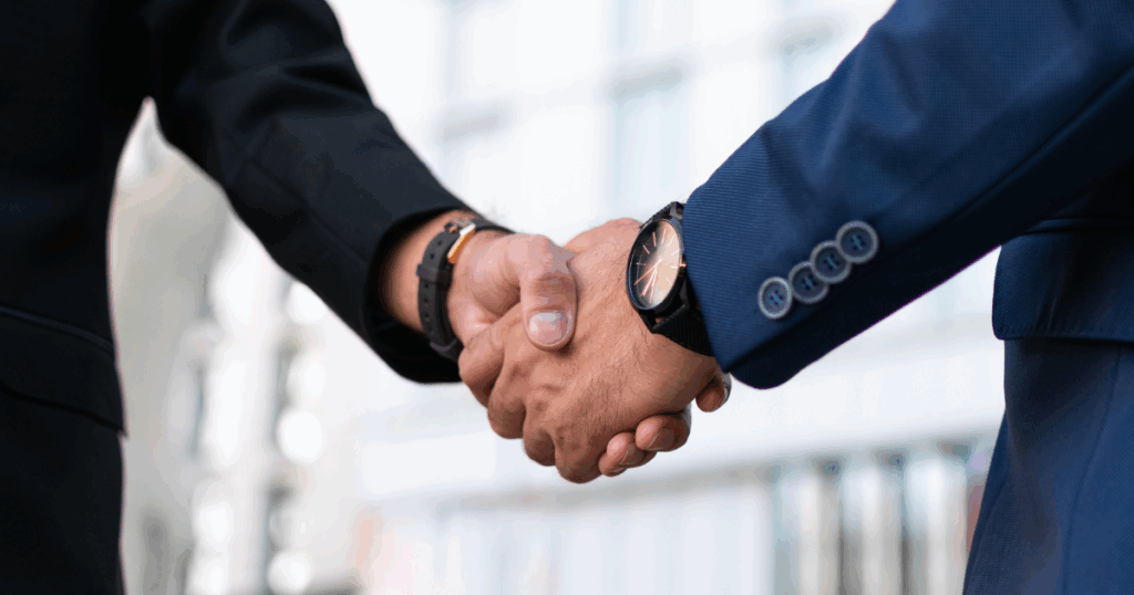 Dois homens de terno apertando as mãos, simbolizando a formalização de um acordo coletivo entre partes profissionais.