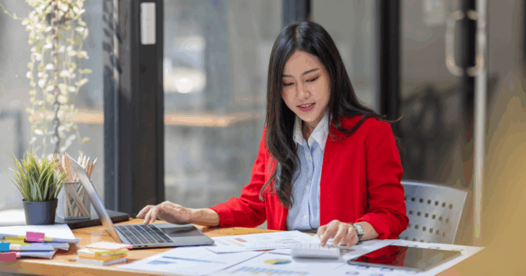 Mulher analisando relatórios financeiros e gráficos em um ambiente de escritório moderno, representando a conferência e organização de dados para elaboração de um balancete.