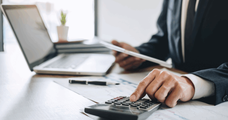 Profissional analisando cálculos fiscais com uma calculadora e uma planilha, enquanto usa um tablet e um laptop, em um ambiente de trabalho, representando a gestão de impostos como o ICMS.