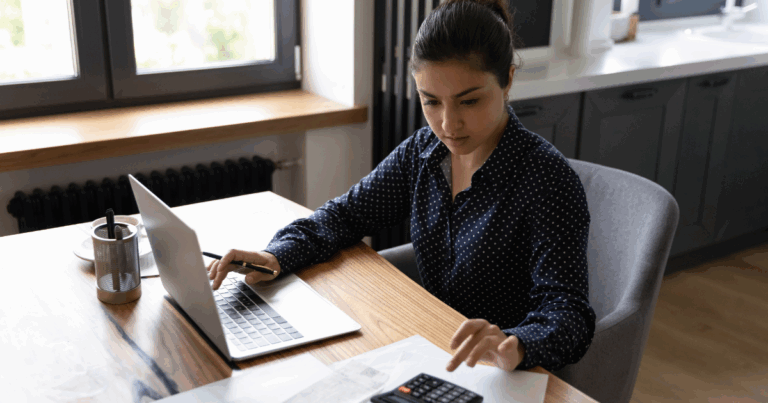 Mulher utilizando uma calculadora e o notebook para declarar o imposto de renda 2025
