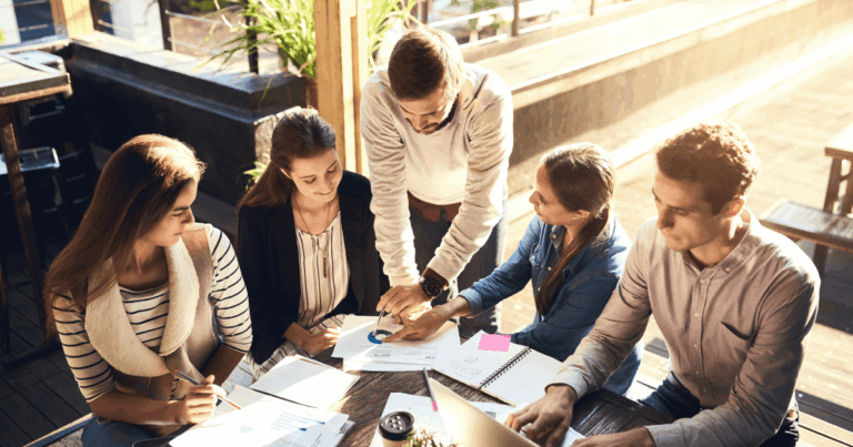 Equipe colaborando em uma reunião ao ar livre, discutindo gráficos e estratégias em papéis e computadores, simbolizando o processo de mudança organizacional e adaptação a novas práticas empresariais