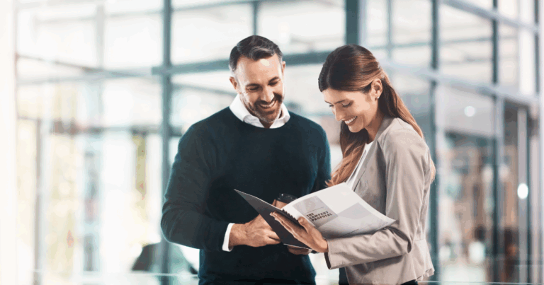 Dois profissionais sorrindo enquanto analisam documentos corporativos em um ambiente empresarial moderno, representando práticas de self compliance no dia a dia das organizações.