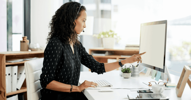 Mulher trabalhando em escritório moderno com headset, usando computador desktop analisando cobrança bancária.