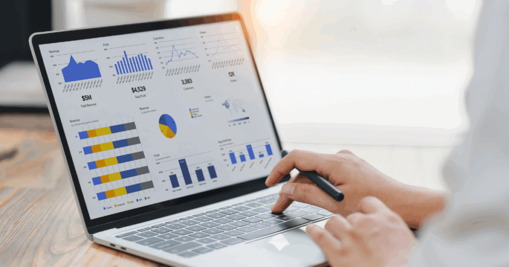 Pessoa analisando gráficos e indicadores em um notebook com dashboard financeiro empresarial, visualizando receitas, lucros, clientes e desempenho por canal de vendas.