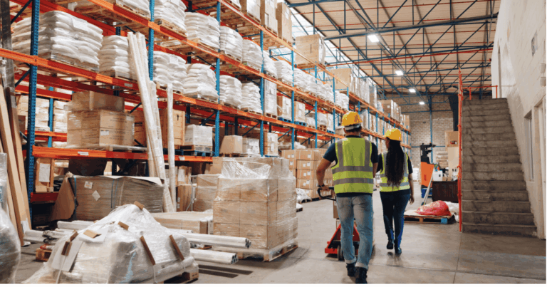 Armazém organizado com prateleiras altas cheias de produtos embalados e funcionários usando coletes refletivos e capacetes, ilustrando a aplicação de princípios da lean logistics para eficiência e otimização de processos.