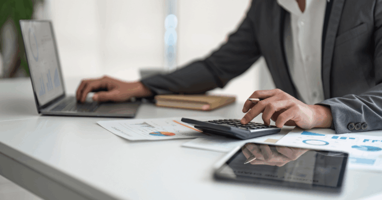 Profissional utilizando calculadora e notebook para analisar gráficos financeiros e relatórios, demonstrando práticas de controle de despesas no ambiente corporativo.