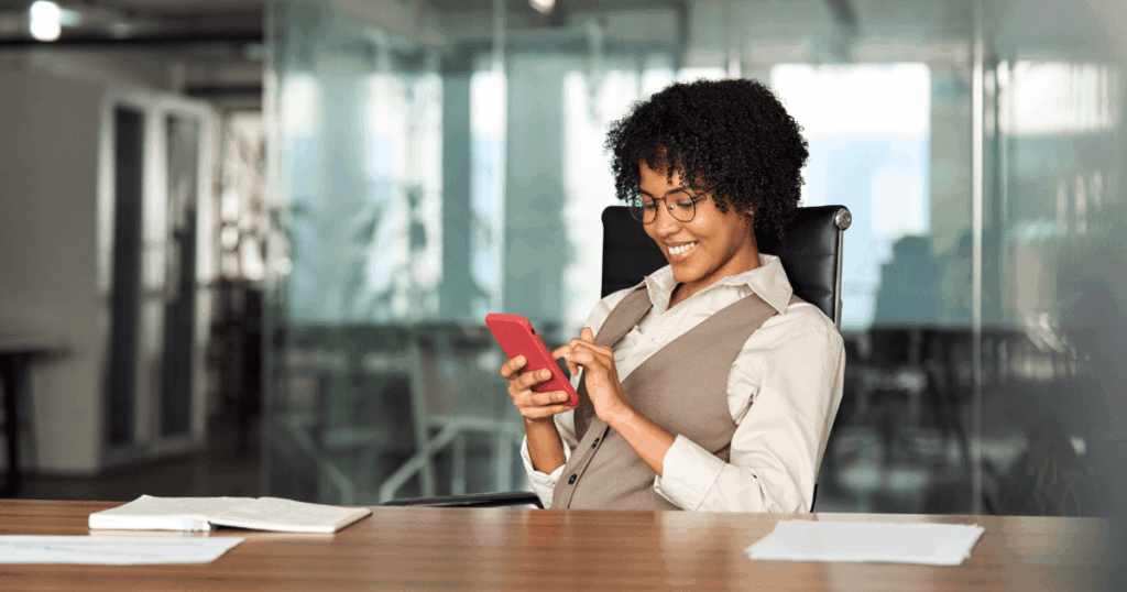 Profissional sorrindo enquanto utiliza o celular em um ambiente de escritório, representando a interação com mensagens automáticas no WhatsApp.