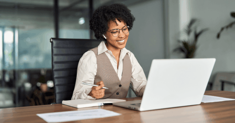 Profissional sorrindo durante reunião one a one online, com notebook, anotações e fone de ouvido, representando a prática de 1:1 nas empresas.