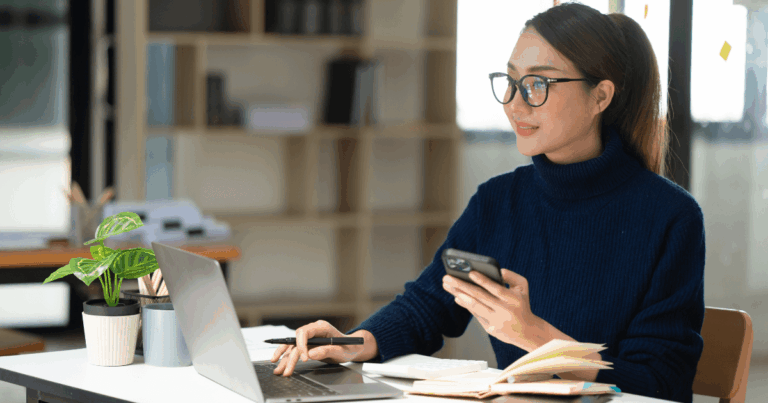 Profissional com celular em mãos, olhando para o notebook, analisando a diligência em contratos