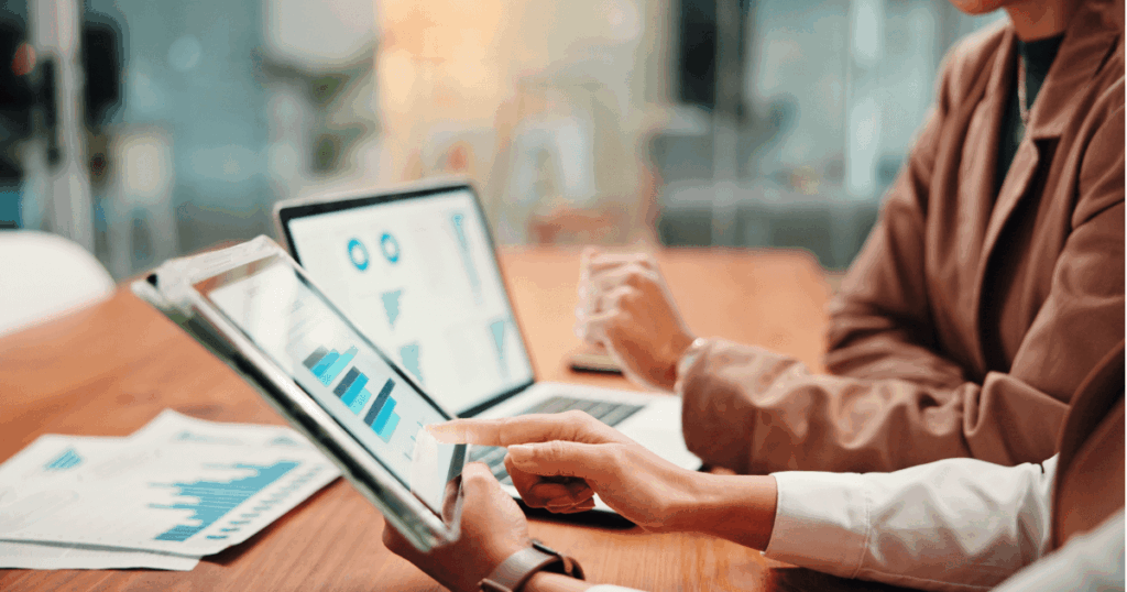 Duas pessoas analisando gráficos financeiros em dispositivos, com foco em dados e análises de gestão financeira.