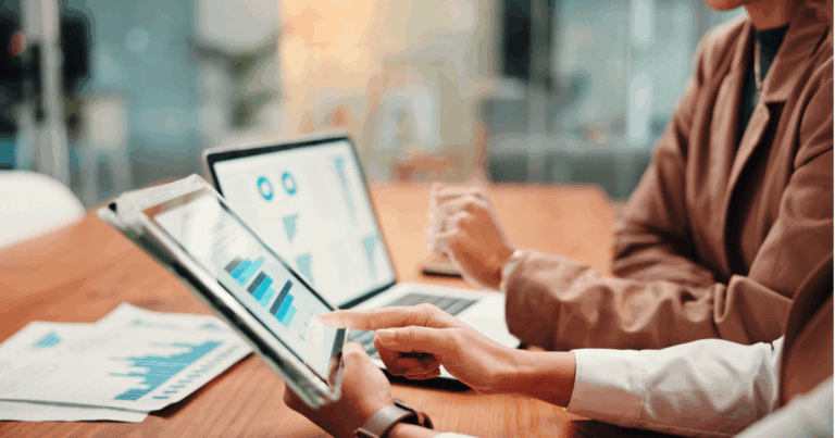 Duas pessoas analisando gráficos financeiros em dispositivos, com foco em dados e análises de gestão financeira.