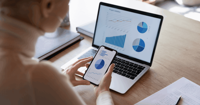 Profissional analisando gráficos sobre o capital de giro no notebook, com celular em mãos.