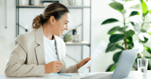 Mulher em um escritório, segurando uma folha de papel e analisando uma matriz de materialidade impressa. Ela aparenta estar concentrada na avaliação de temas relevantes para o negócio e para os stakeholders, em um ambiente profissional.