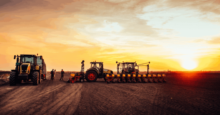 Tratores e equipamentos de plantio alinhados em lavoura ao pôr do sol, representando a mecanização agrícola.