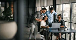 Equipe reunida em um escritório moderno, sorrindo enquanto analisa dados em um notebook, representando o uso colaborativo de um software de RH.
