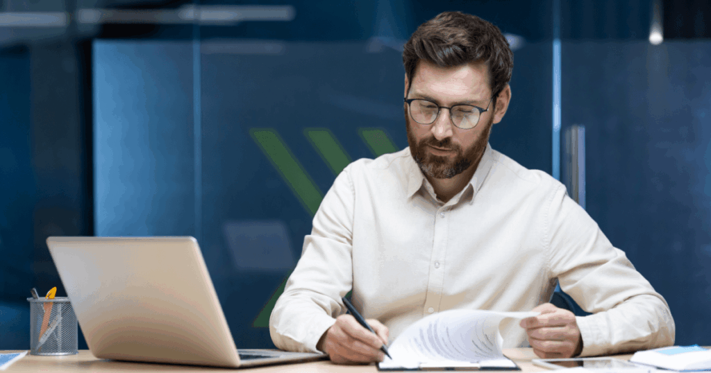 Homem analisando documentos financeiros em um escritório moderno, com notebook aberto sobre a mesa, representando a aplicação das normas do IFRS 16 na gestão contábil.