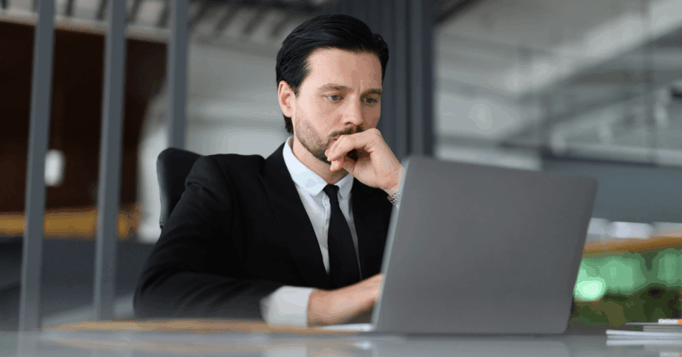 Profissional analisando informações de licitação em um laptop dentro de um ambiente corporativo.