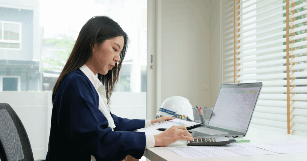 Profissional analisando planilhas no laptop e calculadora em um escritório, ilustrando atividades de contabilidade gerencial.