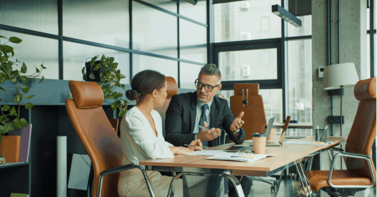 Dois profissionais em um escritório moderno conversam de forma atenta em uma mesa de reunião, representando um momento de feedback contínuo