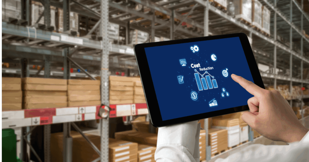 Profissional em centro de distribuição analisando custo de armazenagem em tablet, com gráfico de redução de custos diante de prateleiras com caixas no armazém.