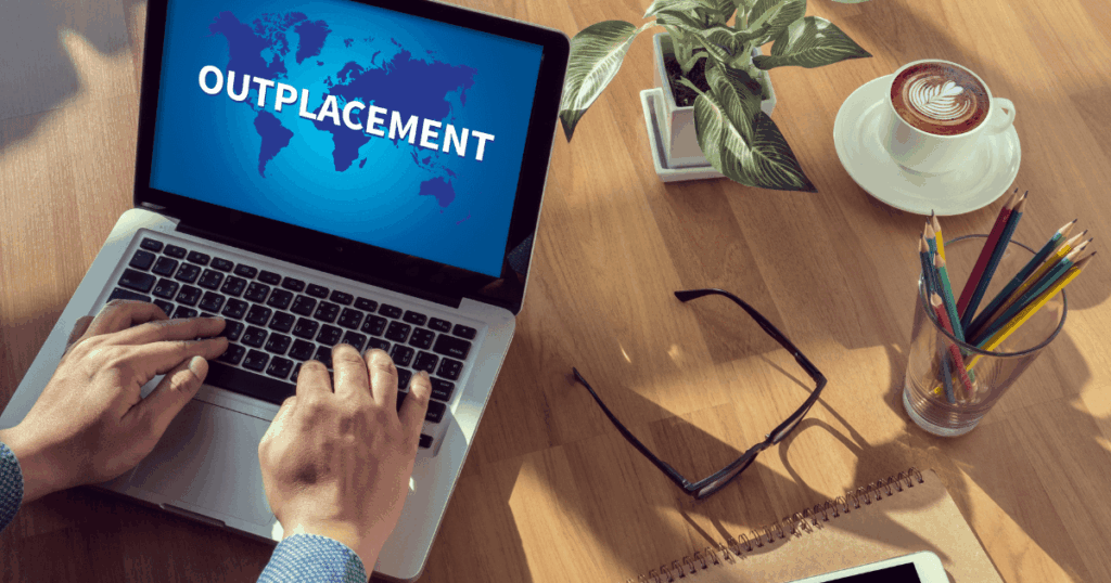 Profissional trabalhando em notebook com a palavra outplacement na tela, representando apoio à transição de carreira e recolocação profissional.