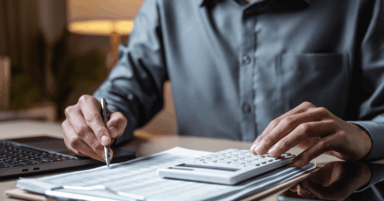 Pessoa analisando documentos financeiros enquanto utiliza calculadora e notebook sobre a mesa, ilustrando o controle e planejamento financeiro baseado em orçamento estático para acompanhamento de despesas e resultados.