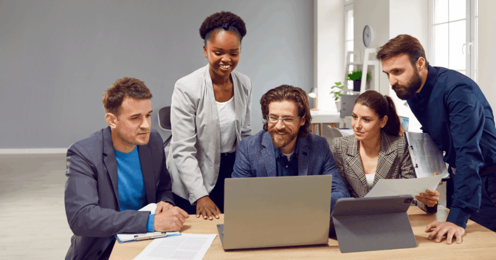 Equipe corporativa colaborando em reunião estratégica ao redor de um laptop, representando Thought Leadership, inovação e tomada de decisão em ambiente profissional.