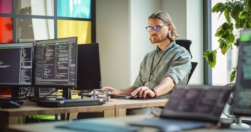 Profissional de tecnologia desenvolvendo projetos open source em computador com múltiplas telas exibindo código, em escritório moderno e colaborativo.