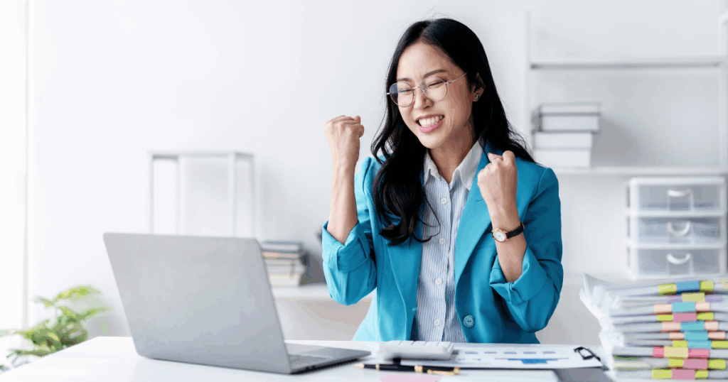 Profissional comemorando uma conquista em frente ao notebook, representando o conceito de bonificação por desempenho no ambiente de trabalho.