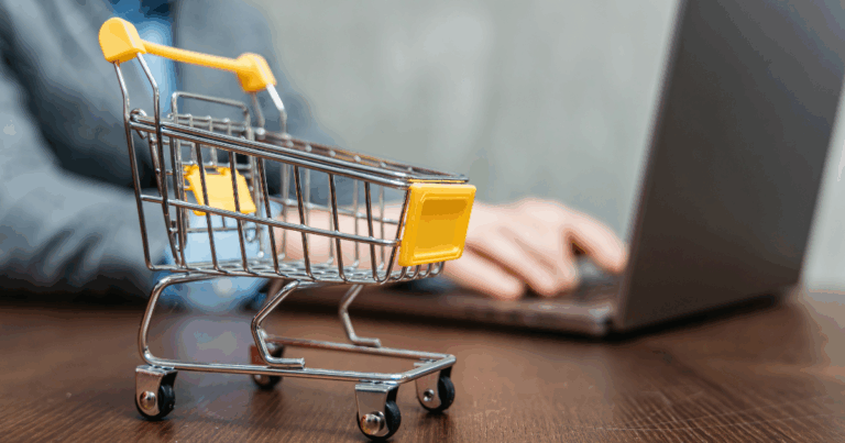 Carrinho de compras vazio em primeiro plano, com uma pessoa usando um notebook ao fundo, representando o conceito de carrinho abandonado em compras online.